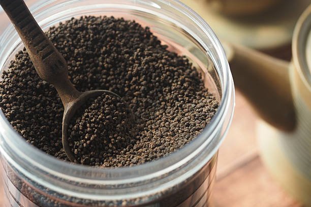 Close view of black tea leaves stored in a container with a scoop nearby.